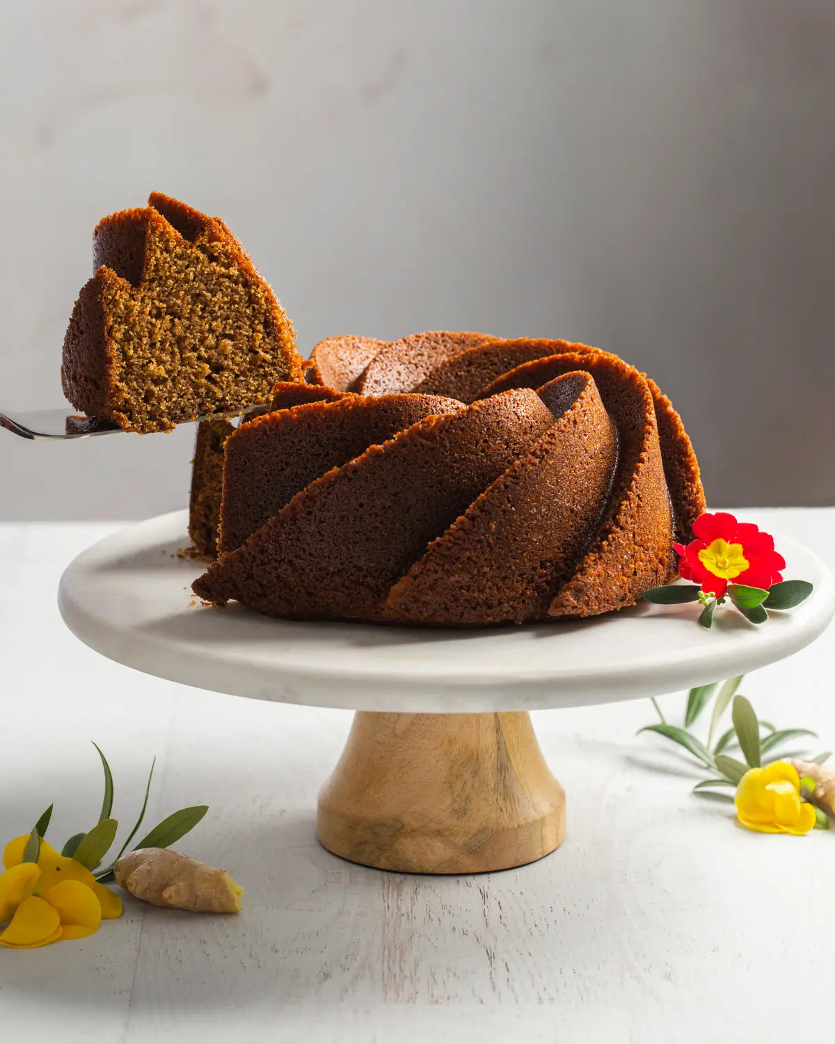 Bundt cake on a marble cake stand with a slice removed, on a light gray background.
