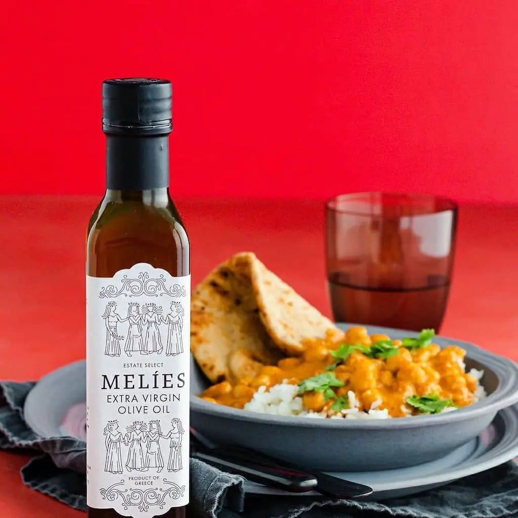 Bottle of Melies Extra Virgin Olive Oil with a dish of curry and naan bread on a red background